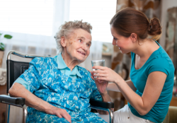 caregiver giving medication to an elderly woman in wheelchair